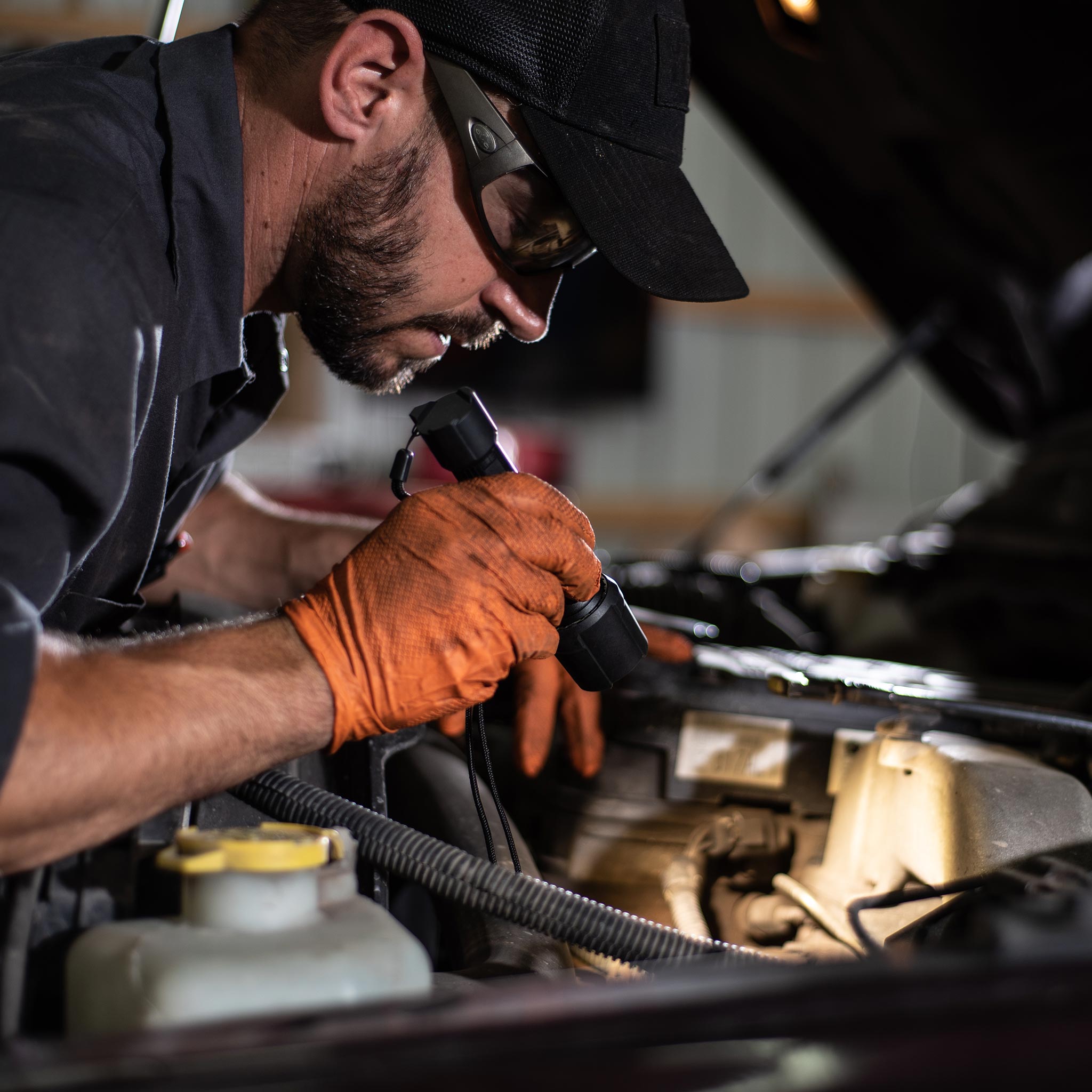P6R Work Torch held by a mechanic under the hood wearing cap and orange gloves inspecting the engine bay