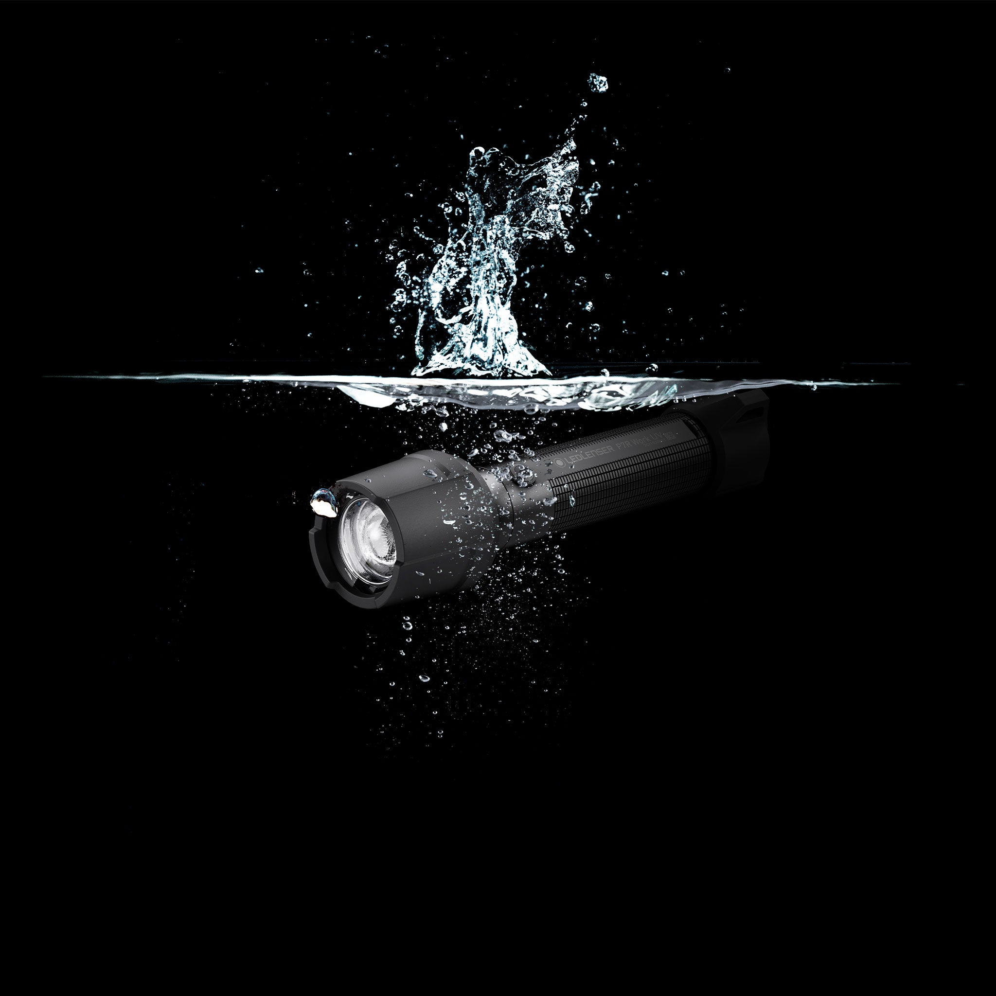 Ledlenser P7R Work UV Torch angled left black cylindrical rechargeable flashlight submerged in water with splash around the head
