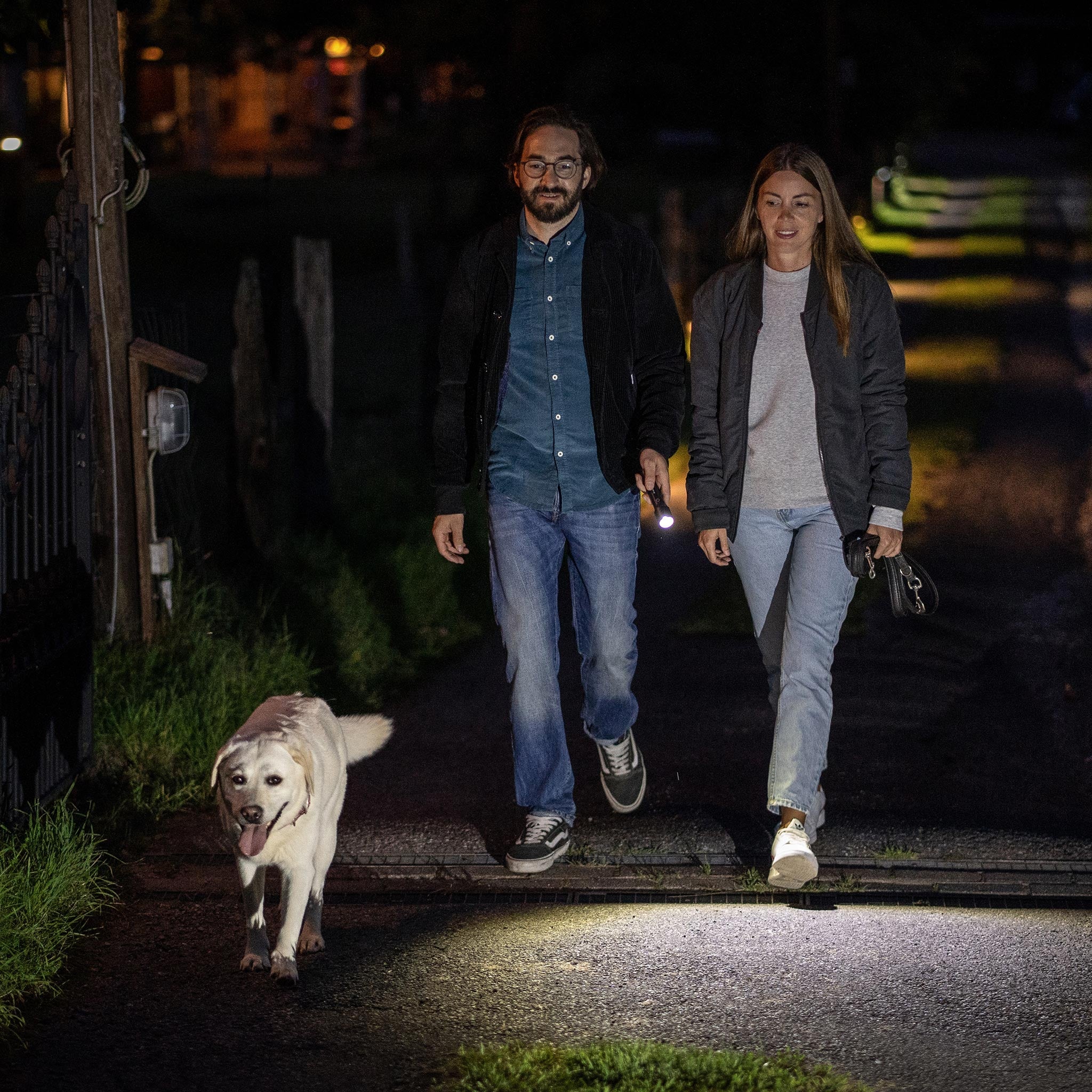 Ledlenser P7R Core Torch held by a man walking a dog on a dim night path with a woman nearby
