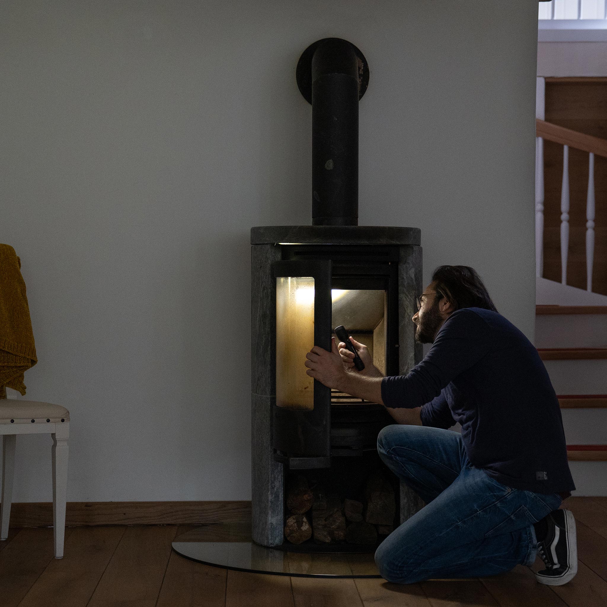 P7R Core Torch held by a man kneeling beside a wood stove in a dim living room with warm stove light