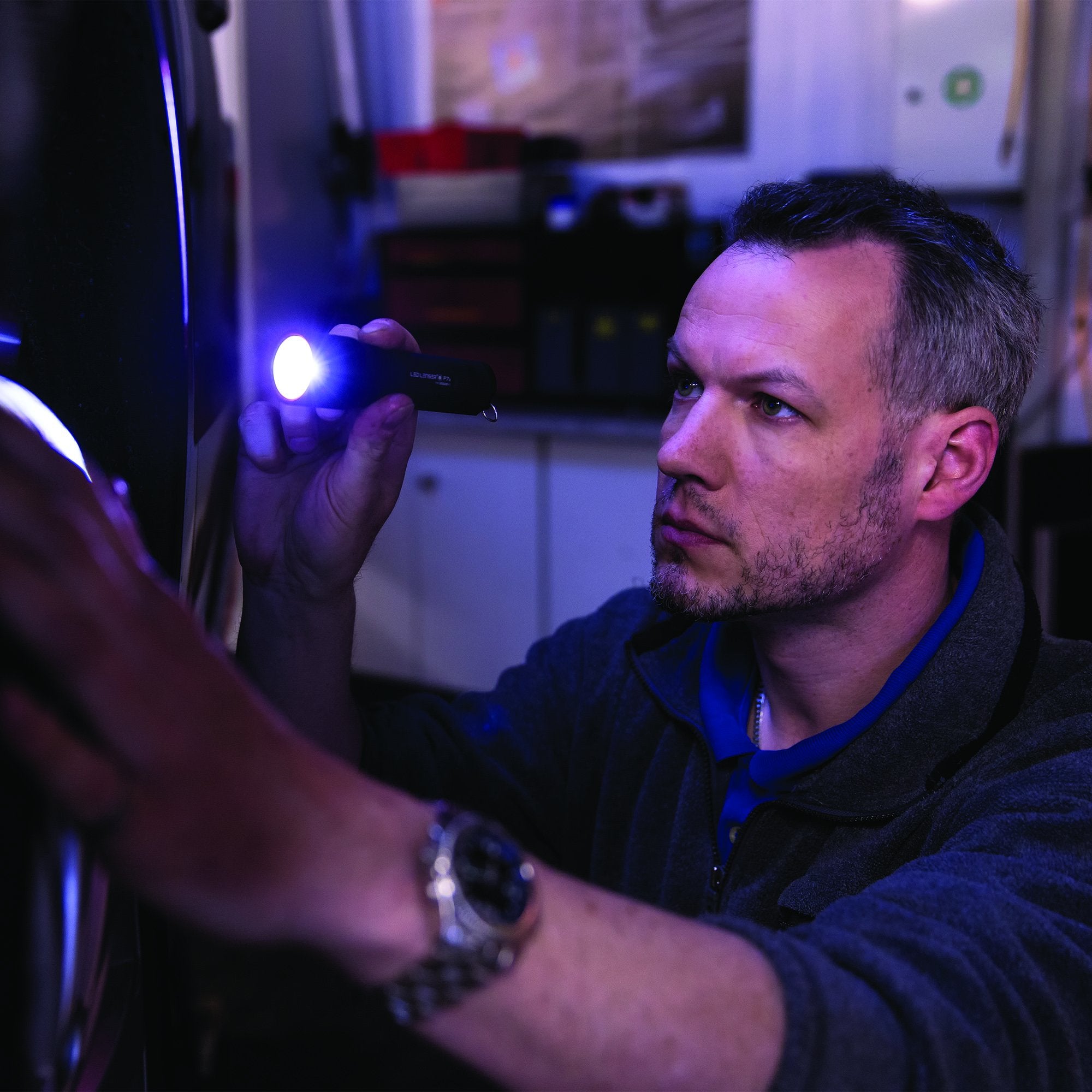 Ledlenser P7 Battery Operated Torch held in the right hand of a man in a workshop emitting blue light onto a wall