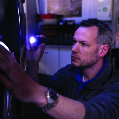 Ledlenser P7 Battery Operated Torch held in the right hand of a man in a workshop emitting blue light onto a wall