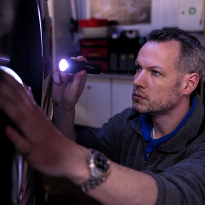 Ledlenser P7R Torch held by a man indoors aimed at a wall with the purple beam visible in a dim workshop