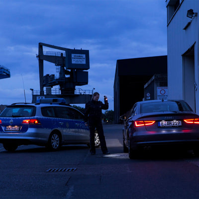 Tac Torch Ledlenser handheld flashlight held up by a person at night between police cars in an industrial area