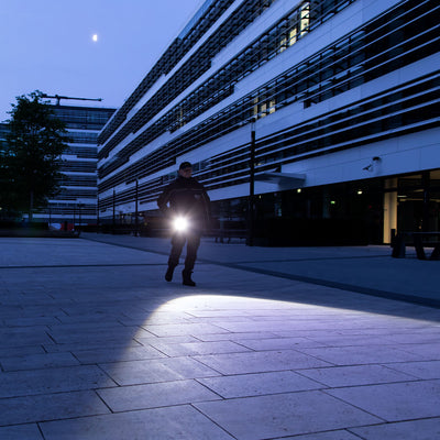 Ledlenser X21R Torch held by a person walking outdoors at night beside a modern building with a bright beam illuminating the pavement
