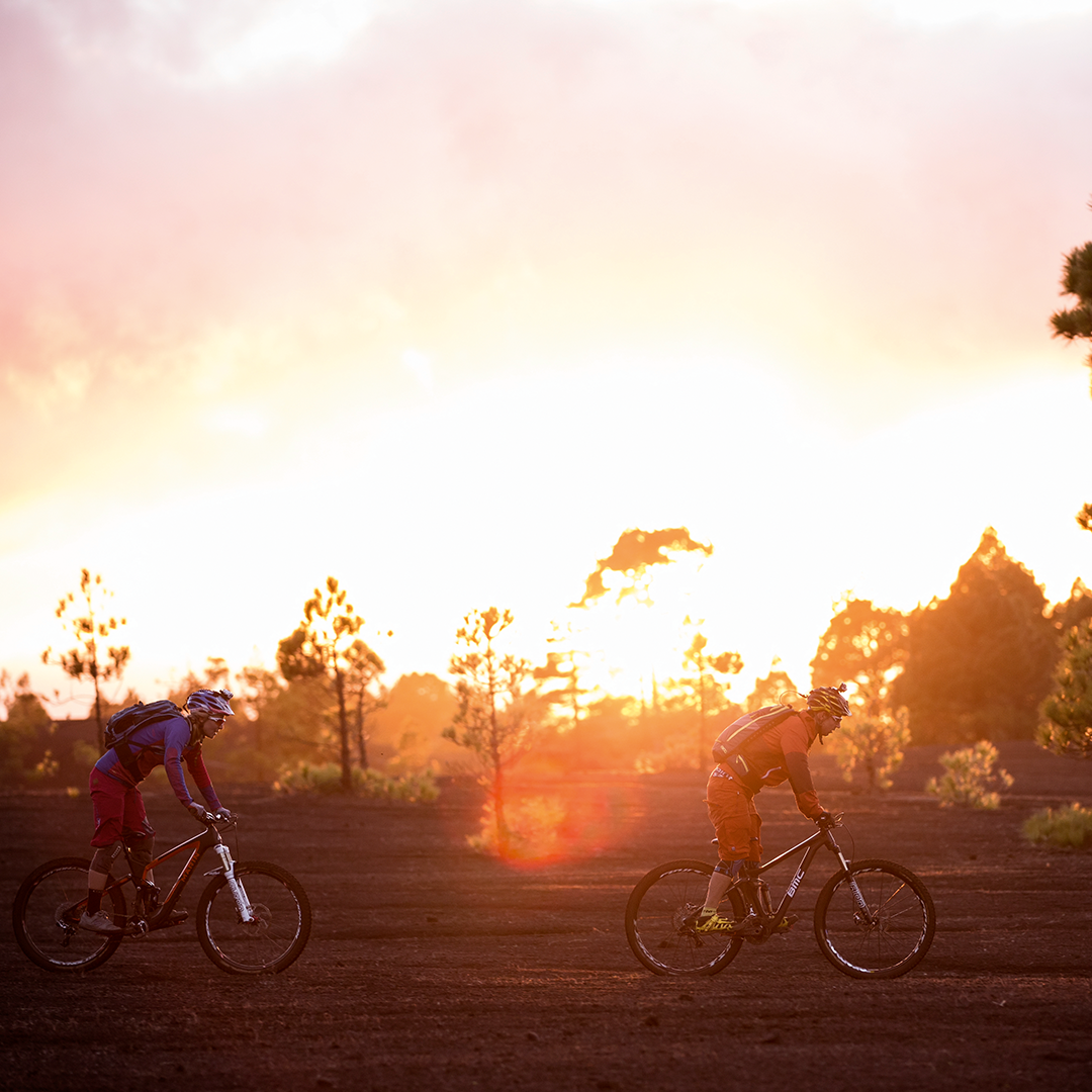 Ledlenser XEO19R White Rechargeable Headlamp two cyclists riding mountain bikes on a dusty trail at sunset warm sky illumination