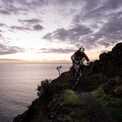 XEO19R Rechargeable Headlamp mounted on a cyclist's helmet during a mountain bike trail at sunset