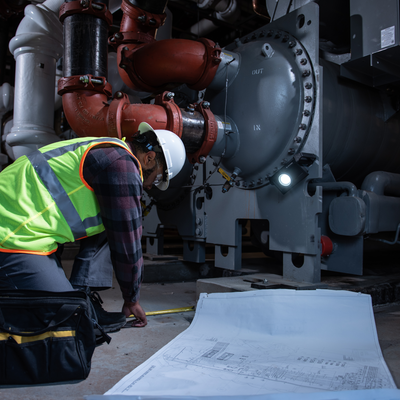 iF4R Music Spotlight with a technician in a high‑visibility vest inspecting large industrial piping and blueprints
