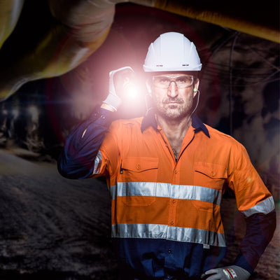 iL7 Torch held by a worker in a white helmet and orange high visibility jacket on a dim industrial site with the light beam visible