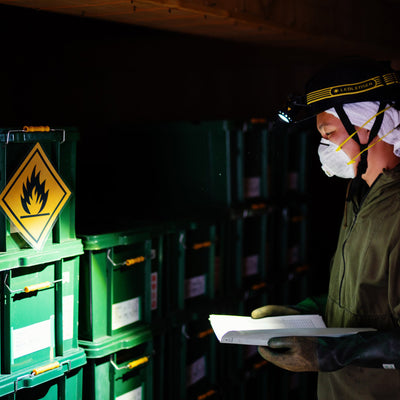 Ledlenser iLH8R Headlamp worn by a worker in safety gear with headlamp on inspecting documents in a dim warehouse with green storage crates