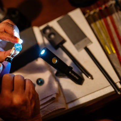 iW4R Work Light being assembled; a hand holds a small blue component beside a black Ledlenser work light with a blue illuminated LED